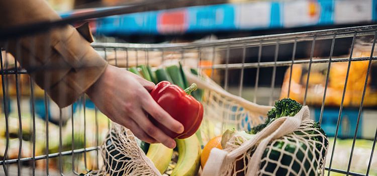 Eine Frau füllt ihren Einkauswagen im Supermarkt mit Gemüse