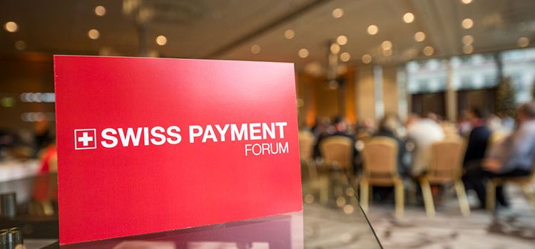 Plakat Swiss Payment Forum, im Hintergrund Tagungsteilnehmer