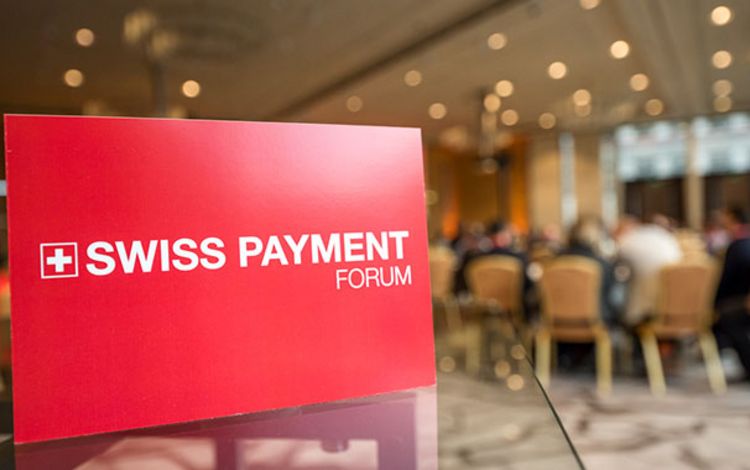 Plakat Swiss Payment Forum, im Hintergrund Tagungsteilnehmer