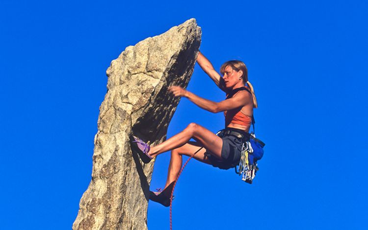 Bergsteigerin in der Felswand vor blauem Himmel