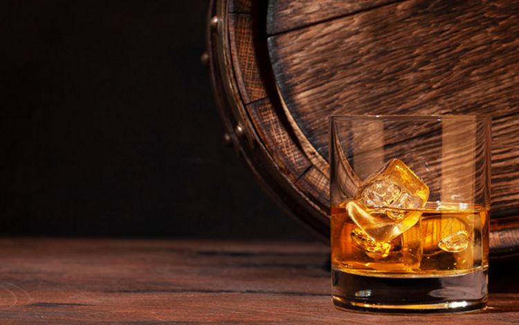 Glas mit Whiskey und ein altes Fass im Hintergrund