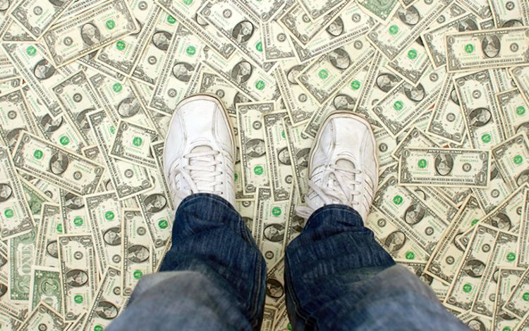 Ein Mann mit Turnschuhen steht auf einem Boden aus Geldscheinen