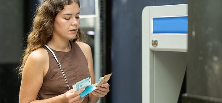 Junge Frau zählt Geld am Geldautomaten