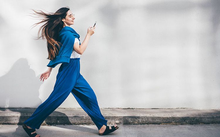 Junge Frau geht sehr schnell und schaut auf ihr Smartphone