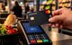 Eine Hand hält eine Mastercard ans Bezahl-Terminal in einem Laden