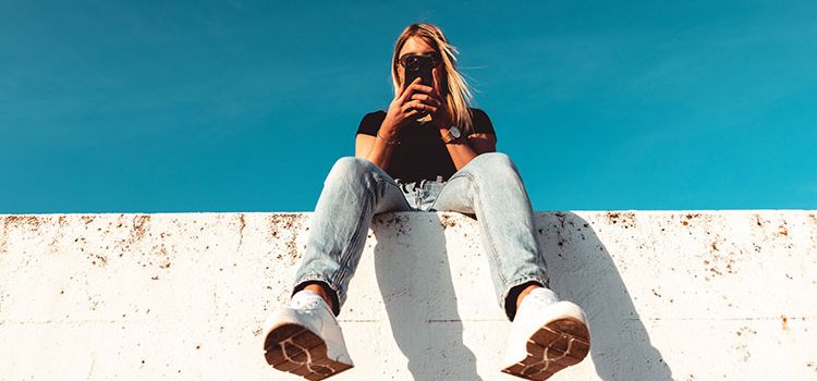 Junge Frau sitzt auf Mauer und checkt ihr Smartphone