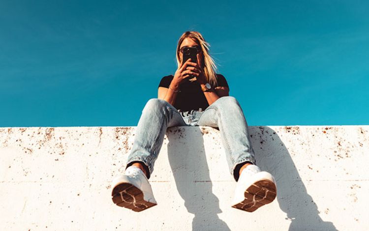 Junge Frau sitzt auf Mauer und checkt ihr Smartphone