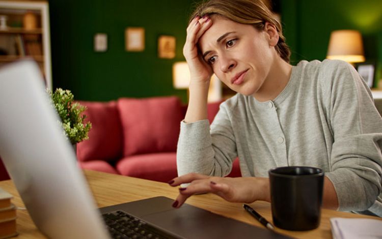 Junge Frau vor dem Laptop ärgert sich beim Betrachten ihres Bankkontoauszuges