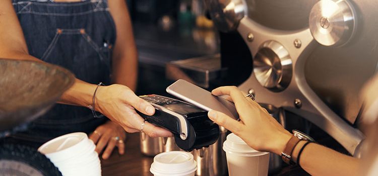 Eine Frau bezahlt ihren Kaffee mit dem Smartphone über Mobile Payment