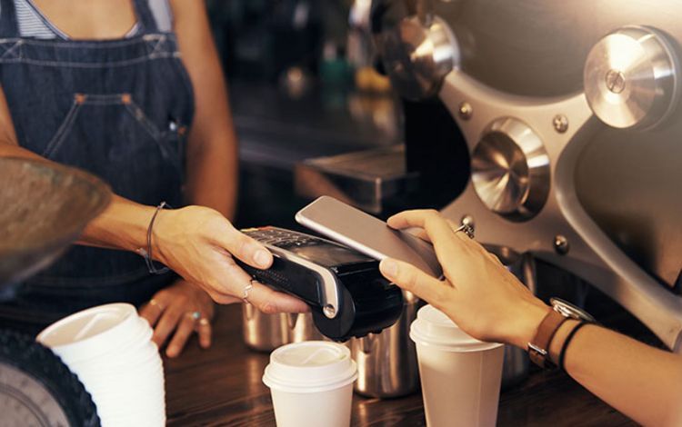 Eine Frau bezahlt ihren Kaffee mit dem Smartphone über Mobile Payment