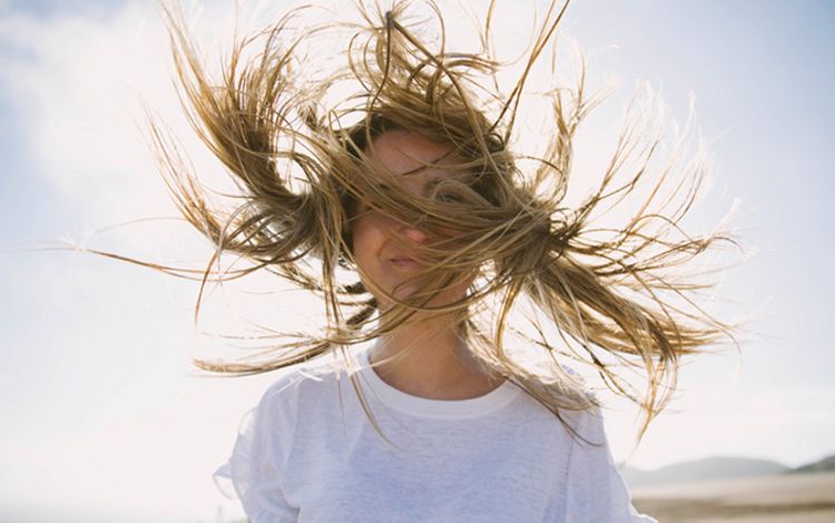 Junge Frau steht im Wind, der ihr die Haare zerzaust