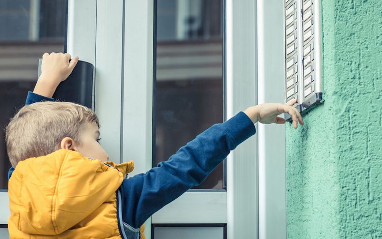 Kind steht am Klingelbrett eines Wohnblocks