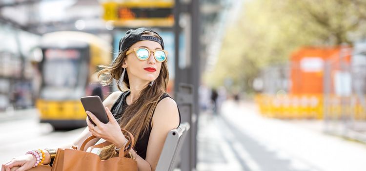 Junge Frau mit Smartphone an Bushaltestele