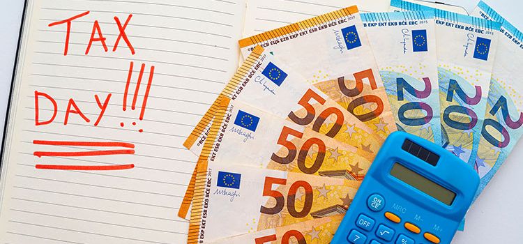 Agenda mit Eintrag Tax Day sowie Taschenrechner und Euroscheine auf dem Schreibtisch