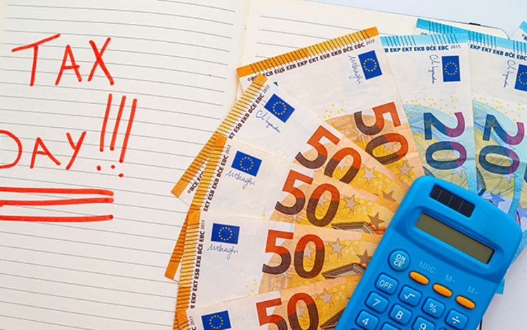 Agenda mit Eintrag Tax Day sowie Taschenrechner und Euroscheine auf dem Schreibtisch