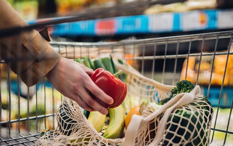 Eine Frau füllt ihren Einkauswagen im Supermarkt mit Gemüse