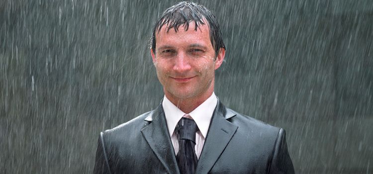 Mann im Anzug steht völlig durchnässt im Regen