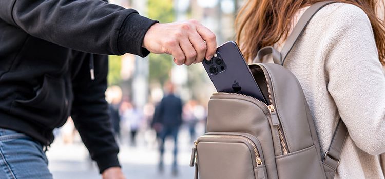 Ein Mann stiehlt einer Frau von hinten das Smartphone aus dem Rucksack
