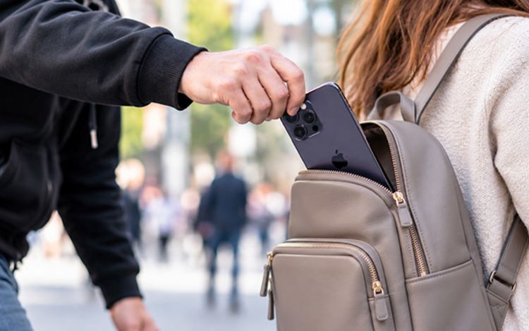 Ein Mann stiehlt einer Frau von hinten das Smartphone aus dem Rucksack