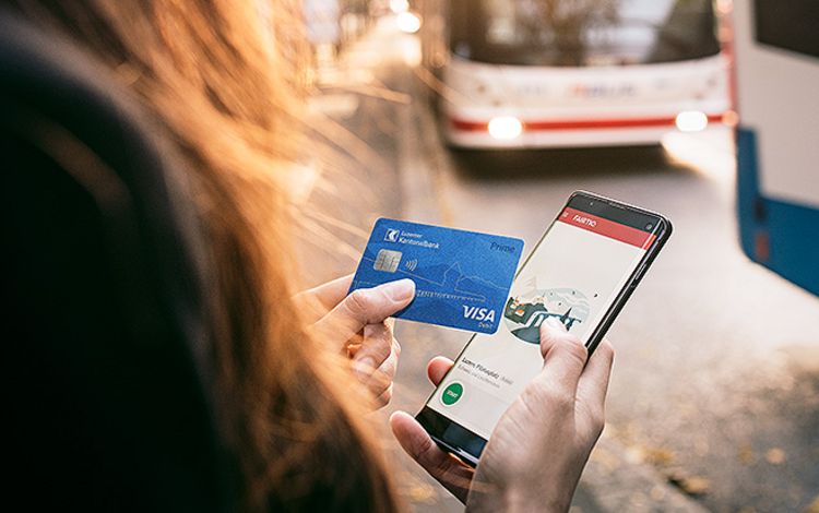 Eine Frau an Bushaltestelle mit Debitkarte und Smartphone in der Hand