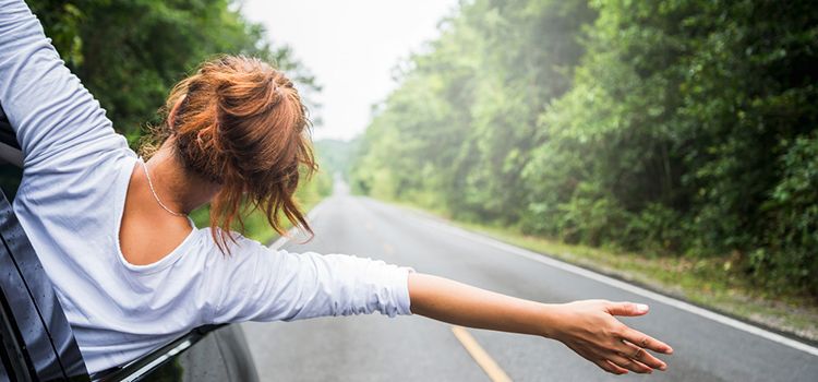 Junge Frau unterwegs im Auto, winkt aus dem Autofenster