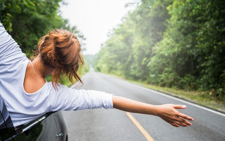 Junge Frau unterwegs im Auto, winkt aus dem Autofenster