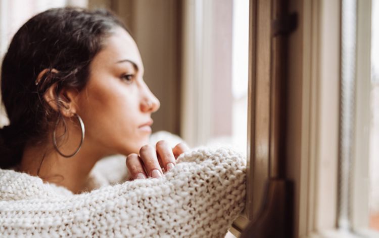 Junge Frau schaut nachdenklich aus dem Fenster