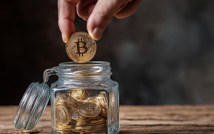 Mann wirft eine Bitcoin-Münze in eine Spardose