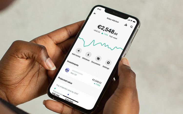 Eine Frau mit Smartphone in der Hand prüft den Robo Advisor in ihrer App