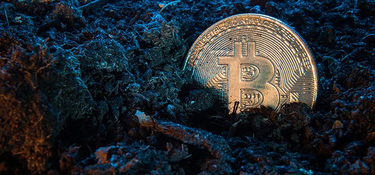 Bitcoin-Münze im Erdreich, als Symbol für Bitcoin Mining