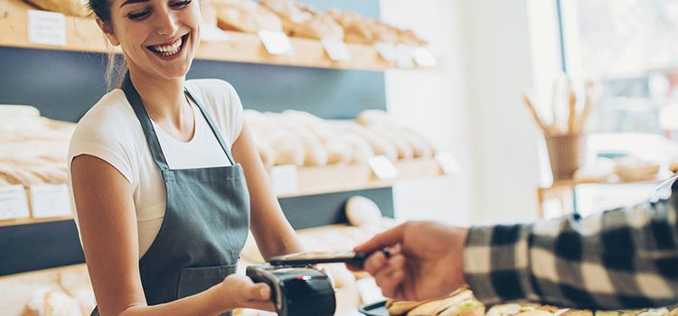 Junge Frau nimmt in der Bäckerei eine Smartphone-Zahlung entgegen