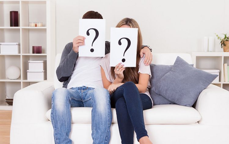 Paar auf Sofa mit Fragezeichen vor dem Kopf