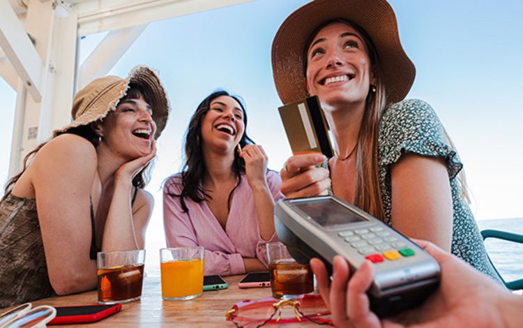 Drei junge Frauen im Urlaub beim Zahlen mit Kreditkarte