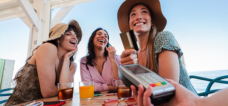 Drei junge Frauen im Urlaub beim Zahlen mit Kreditkarte