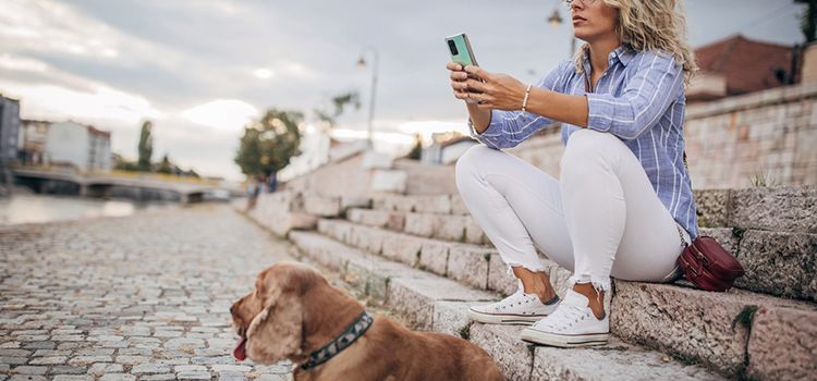 Junge Frau mit Hund studiert am Flussufer ihr Smartphone