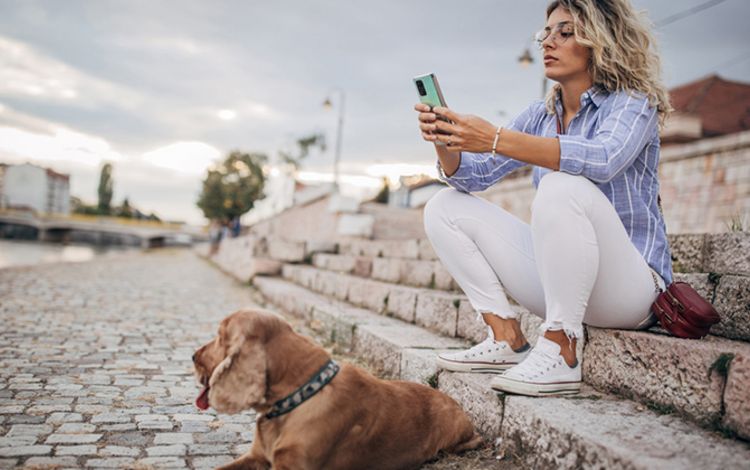 Junge Frau mit Hund studiert am Flussufer ihr Smartphone