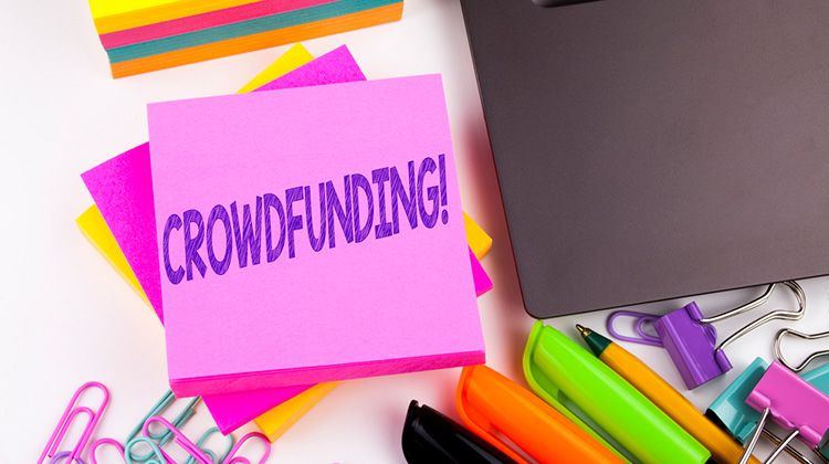 Schreibtisch mit Zettel mit Aufschrift Crowdfunding