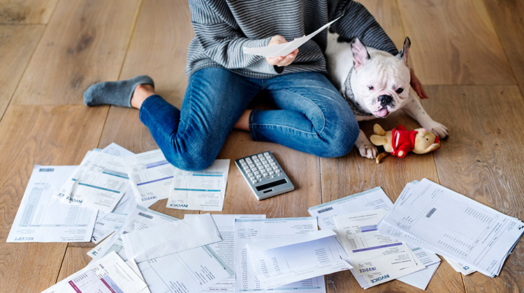 Frau mit Hund sortiert ihre Rechnungen auf dem Wohnzimmerboden