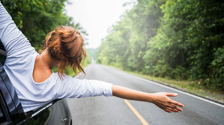 Junge Frau unterwegs im Auto, winkt aus dem Autofenster