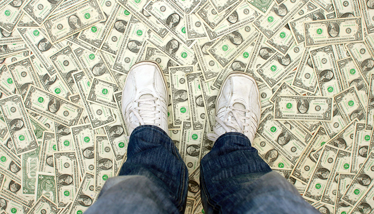 Ein Mann mit Turnschuhen steht auf einem Boden aus Geldscheinen