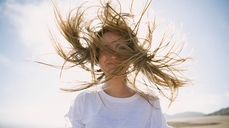 Junge Frau steht im Wind, der ihr die Haare zerzaust