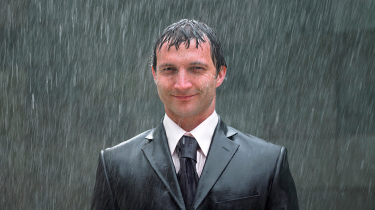 Mann im Anzug steht völlig durchnässt im Regen