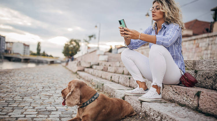 Junge Frau mit Hund studiert am Flussufer ihr Smartphone