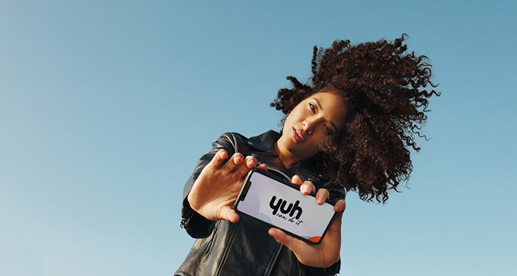 Eine junge Frau hält das Smartphone mit dem Logo der Neo-Bank Yuh in die Kamera