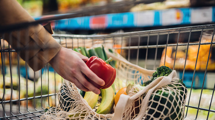 Eine Frau füllt ihren Einkauswagen im Supermarkt mit Gemüse