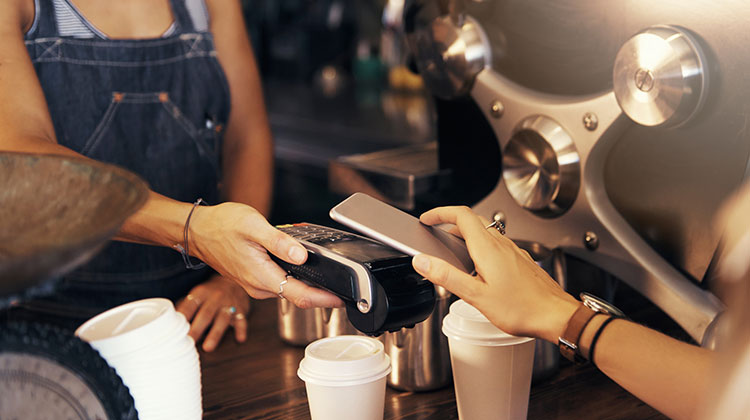 Eine Frau bezahlt ihren Kaffee mit dem Smartphone über Mobile Payment