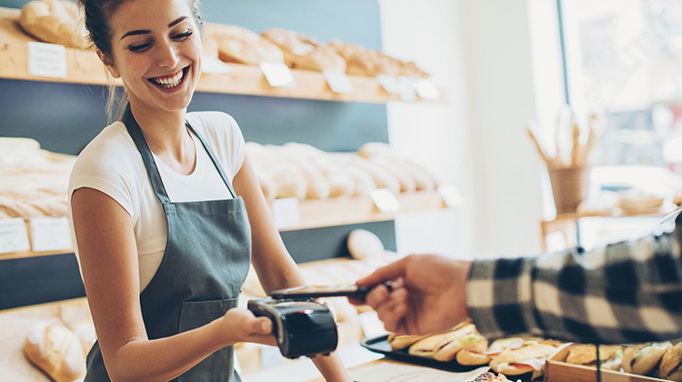 Junge Frau nimmt in der Bäckerei eine Smartphone-Zahlung entgegen