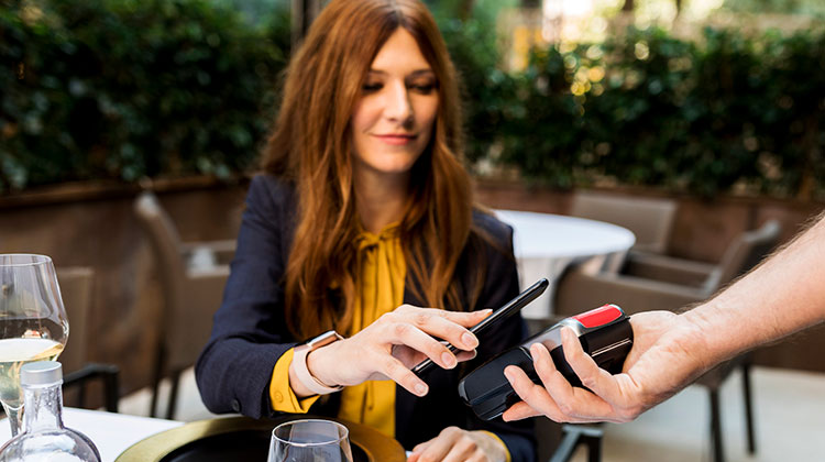 Junge Frau beim kontaktlosen Bezahlen mit dem Smartphone