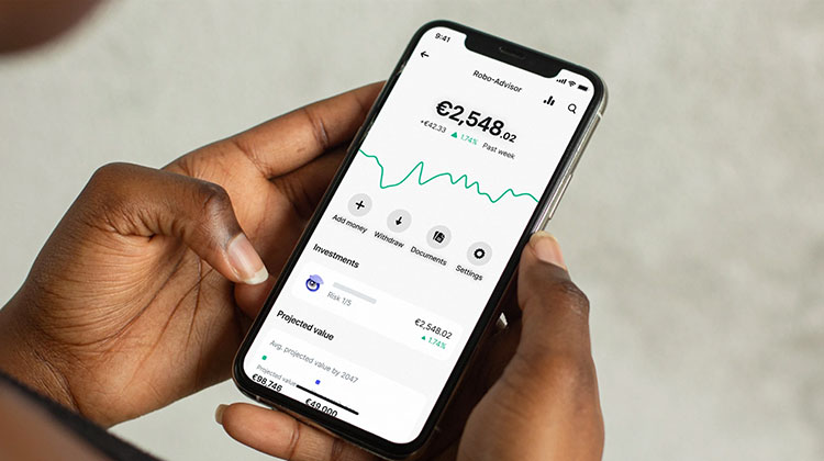 Eine Frau mit Smartphone in der Hand prüft den Robo Advisor in ihrer App