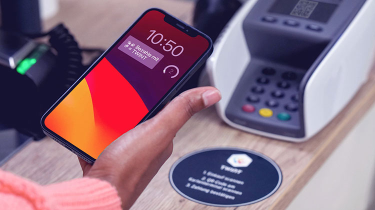 Frauenhand mit Smartphone bezahlt an der Ladenkasse mit Twint Widget